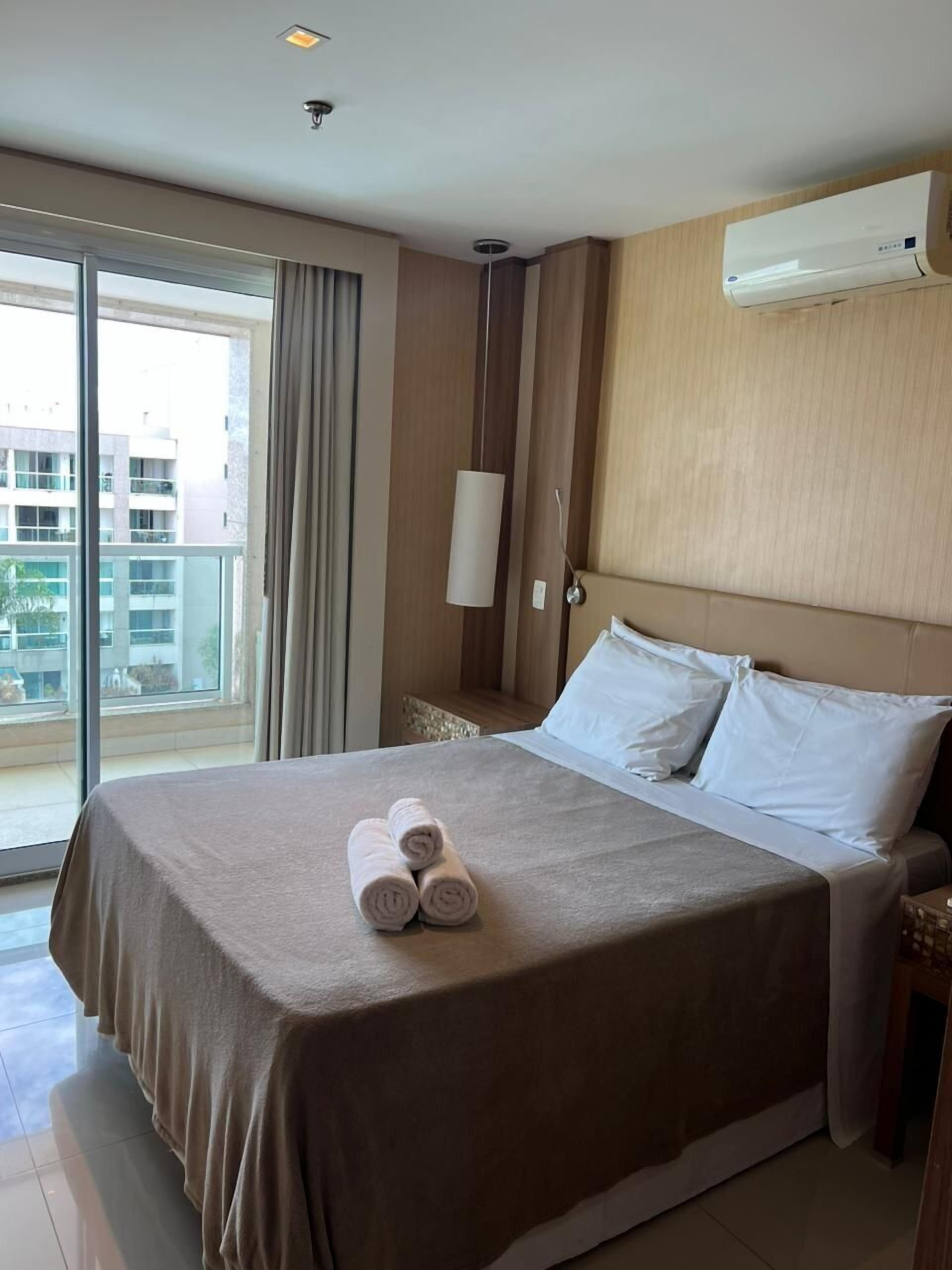 Ein Hotelzimmer mit einem großen Bett, Blick auf die Stadt durch das Fenster und einer Klimaanlage an der Wand.