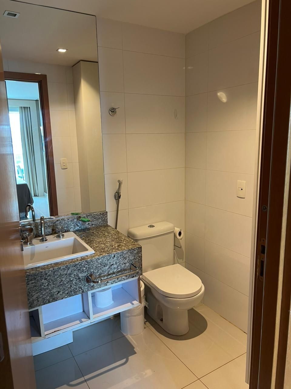 A bathroom with a granite countertop sink, a toilet, and a shower area.