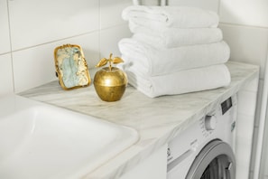 A bathroom with a white sink, a gold decorative item, and a stack of white towels on a marble countertop. - Peaceful 1BR in Design District (Helsinki)