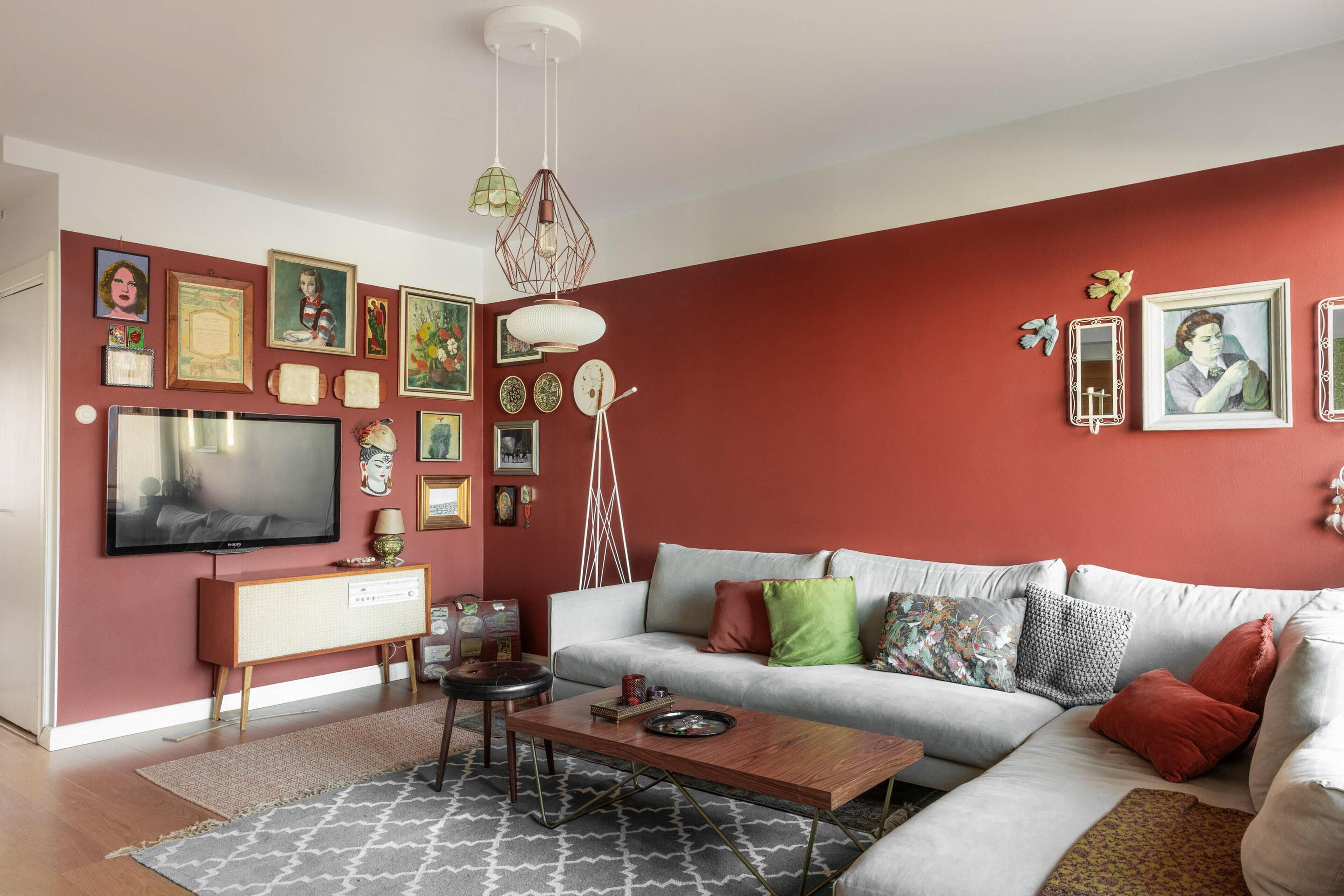 Ein Wohnzimmer mit roter Akzentwand, einem weißen Sofa, einem Holztisch und einem Fernseher auf einem Standfuß.