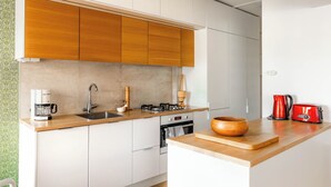 Une cuisine moderne avec des meubles blancs, un plan de travail en bois, une machine à café, un grille-pain et un saladier en bois.