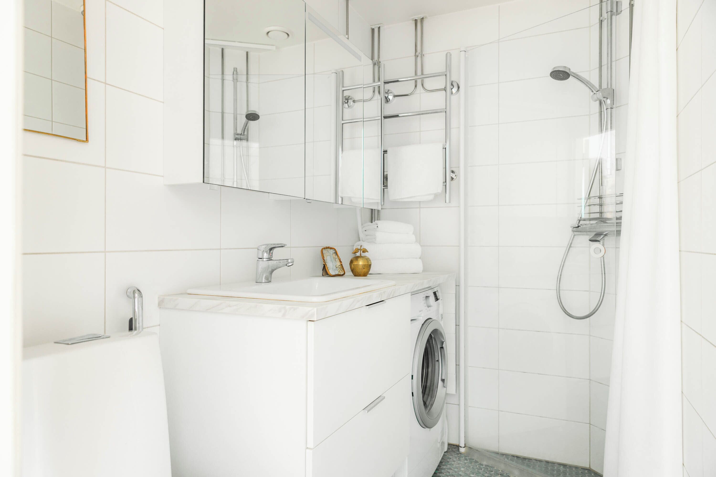A modern bathroom with a built-in washing machine, a shower with a glass door, and a mirror above the sink.