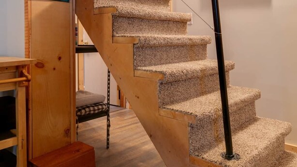 Eine hölzerne Treppe mit Teppichstufen und einem schwarzen Geländer, die zu einer oberen Etage führt.