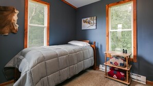 Ein Schlafzimmer mit einem Bett, zwei Fenstern, einem Gemälde und einem Fellkopf an der Wand.
