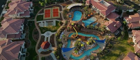 Vista aérea de un resort con varias piscinas, un tobogán de agua y una cancha de tenis.