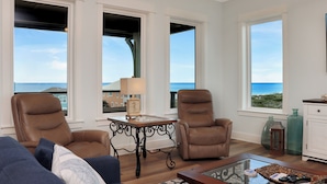 A living room with two leather chairs, a glass coffee table, and a view of the ocean through large windows. - 5BR, Beach View, Elevator, Comm Pool, North Cape (Cape San Blas)