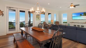 A dining area with a wooden table, benches, and chairs, a ceiling fan, and a large window with a view of the ocean. - 5BR, Beach View, Elevator, Comm Pool, North Cape (Cape San Blas)