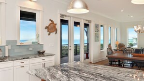 A kitchen with white cabinets, a marble countertop, and a view of the ocean through sliding glass doors. - 5BR, Beach View, Elevator, Comm Pool, North Cape (Cape San Blas)