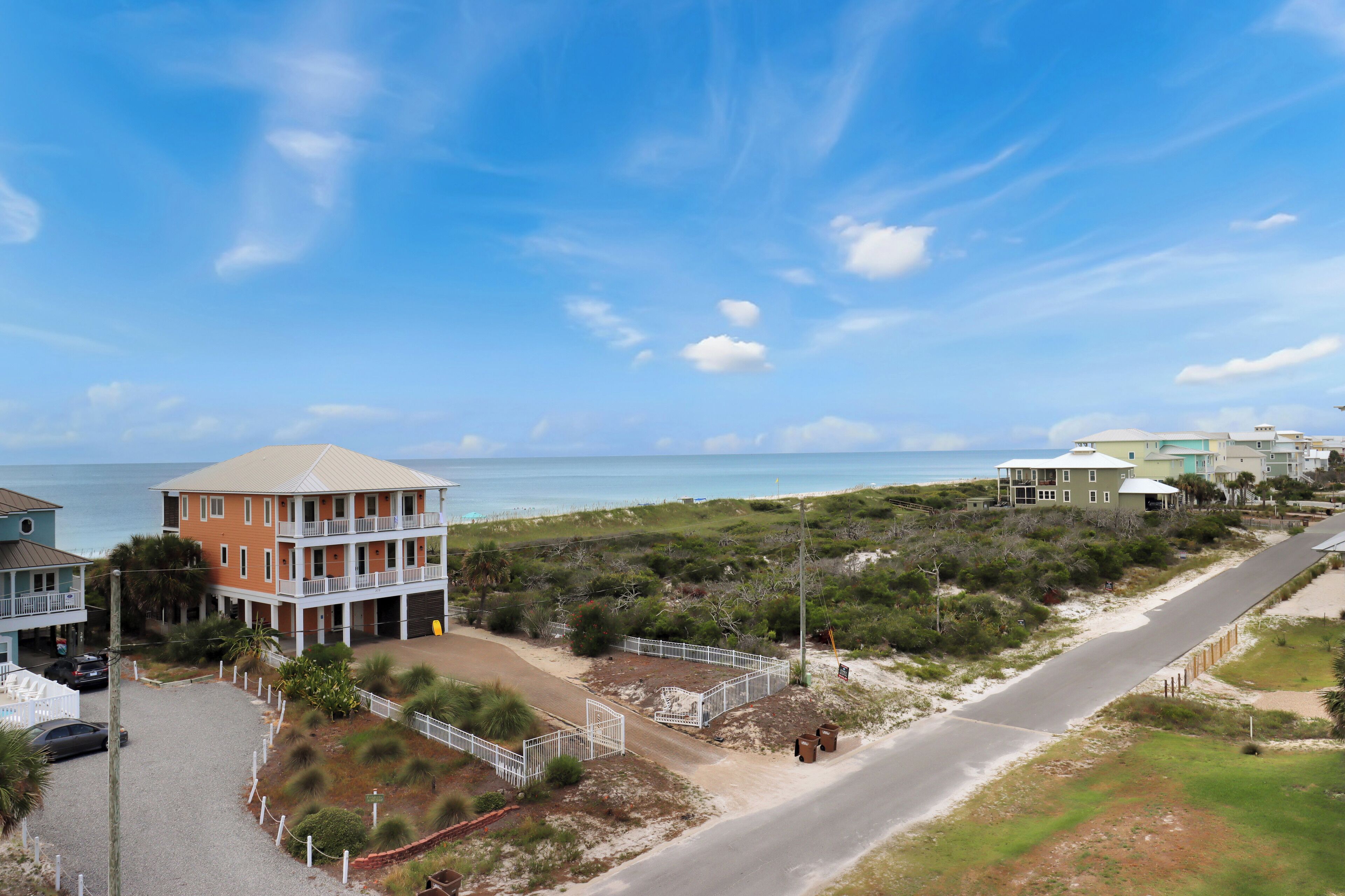 Een hotel aan de kust met meerdere verdiepingen, uitzicht op het strand en een parkeerplaats.