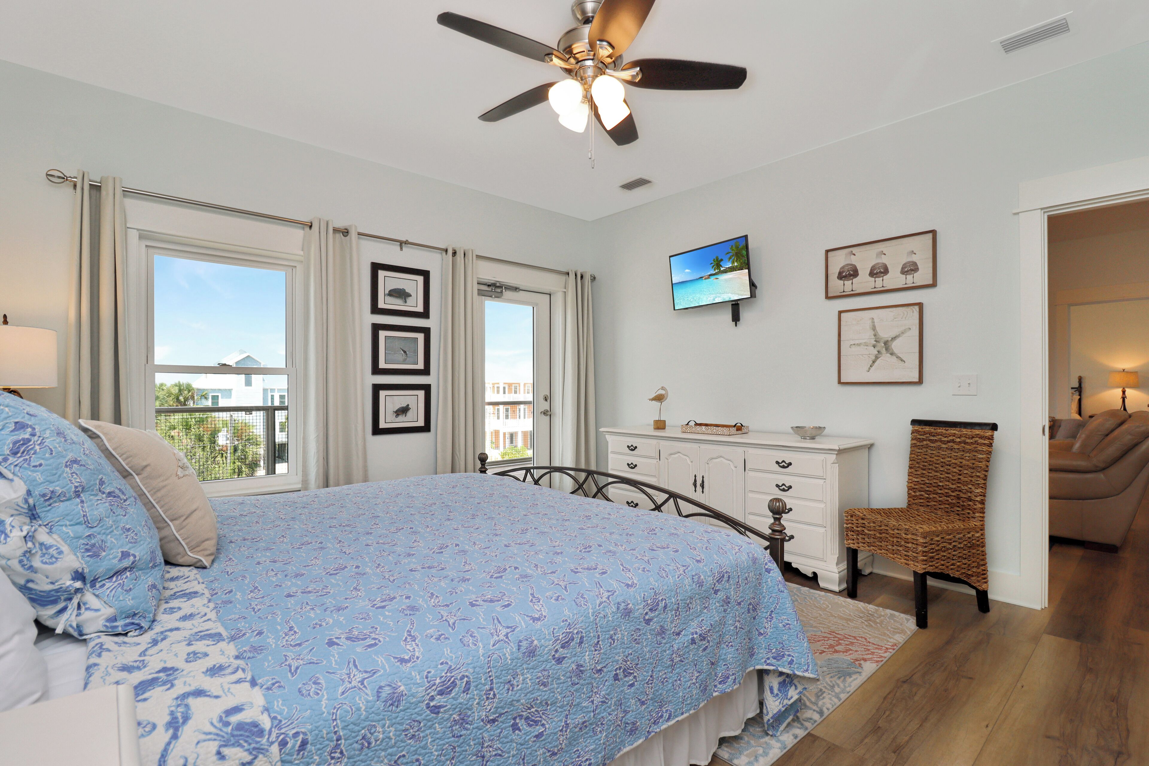 A bedroom with a bed, a ceiling fan, a dresser, a chair, and a television on the wall.