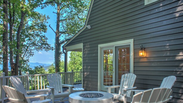 Une terrasse dotée de chaises Adirondack et d’un foyer, offrant une vue sur un plan d’eau et des arbres.