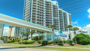 Een hoog hotel met een opvallend bord 'Surfside Royal Palm', meerdere balkons en een goed onderhouden gazon met palmstruiken.