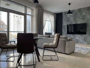 Ein modernes Wohnzimmer mit einer Couch, zwei Sesseln, einem Couchtisch und einem an der Wand montierten Fernseher.