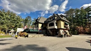 Un chalet à deux étages, doté de fondations en pierre et d’un toit végétalisé, entouré d’arbres et surplombant un ciel dégagé.
