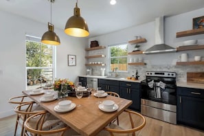 Une cuisine moderne avec des meubles de couleur sombre, une table à manger en bois et des luminaires suspendus.