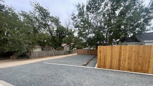 Un camino de acceso residencial con superficie de grava, cerca de madera y casas al fondo.
