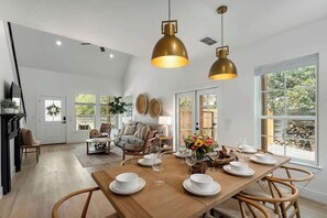 Un comedor con una mesa de madera dispuesta para seis personas, rodeada de sillas de mimbre, bajo dos lámparas colgantes de latón.