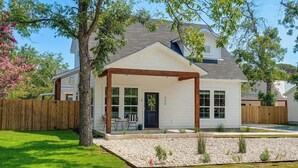 Une maison de plain-pied avec un porche couvert, une petite cour avec un arbre et un petit jardin, et une clôture en bois.