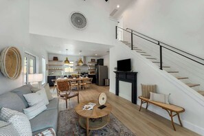 A spacious living area with a sofa, coffee table, and a staircase leading to an upper floor. - The Rosé: Hot-Tub + Firepit 3 Blks to Main Street! (Fredericksburg)