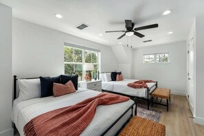 Une chambre avec deux lits, un ventilateur de plafond et une grande fenêtre.