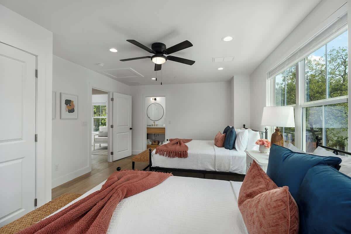 A modern bedroom with two beds, a ceiling fan, a large window, and a view of the outdoors.