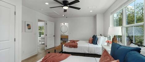 A modern bedroom with two beds, a ceiling fan, a large window, and a view of the outdoors.