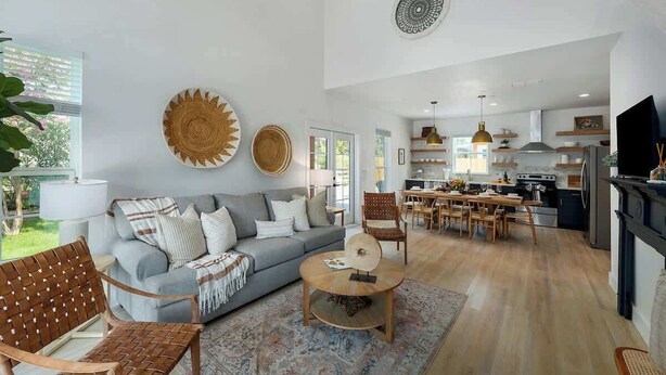 Un vaste espace de vie comprenant un canapé gris, une table basse en bois et un coin repas avec une table et des chaises en bois.