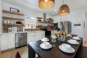 Une cuisine moderne avec des meubles blancs, un lave-vaisselle en acier inoxydable et une table à manger agrémentée d’assiettes et de verres blancs.