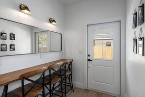 A hallway with a white door, a wooden bench, and a mirror with wall-mounted lights.