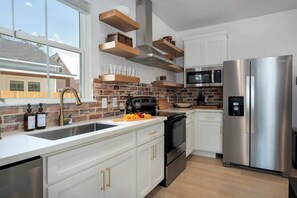 Eine moderne Küche mit weißen Schränken, einem Edelstahl-Kühlschrank, einer Mikrowelle und einer Backspülwand aus Ziegelsteinen.