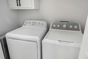 Deux machines à laver à chargement frontal, de couleur blanche, se trouvent dans une buanderie, avec un meuble blanc placé au-dessus.