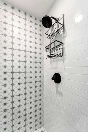 Ein Badezimmer mit weißen, im U-Format verlegten Fliesen und einem geometrischen Sternmuster. An der Wand sind drei schwarze, aus Metall gefertigte Handtuchhalter angebracht.