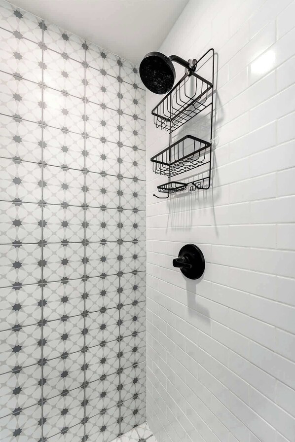 Un baño con azulejos blancos tipo metro y un patrón geométrico de estrellas. Hay tres toalleros metálicos negros fijados a la pared.