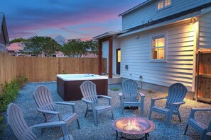 A backyard with Adirondack chairs, a hot tub, and a fire pit.
