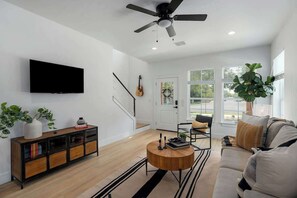 A modern living room with a flat-screen TV, a ceiling fan, a wooden coffee table, a sofa, and a potted plant.