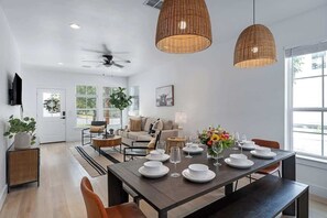 A modern dining area with a dark wooden table set for six, surrounded by chairs. There are two large woven pendant lights above the table.