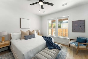 Une chambre à coucher avec un lit, une chaise, un ventilateur de plafond et une fenêtre.