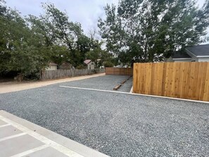 Un camino de acceso residencial con superficie de grava, cerca de madera y casas al fondo.