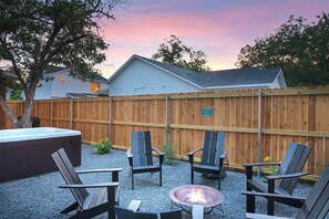 Un jardin avec un jacuzzi, quatre fauteuils Adirondack et un foyer extérieur.