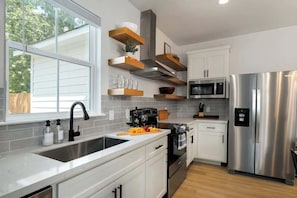 Una cocina moderna con armarios blancos, electrodomésticos de acero inoxidable y estantes de madera.