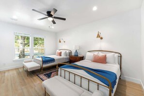 Une chambre avec deux lits, un ventilateur de plafond, des lampes de chevet, une fenêtre et une vue sur l’extérieur.