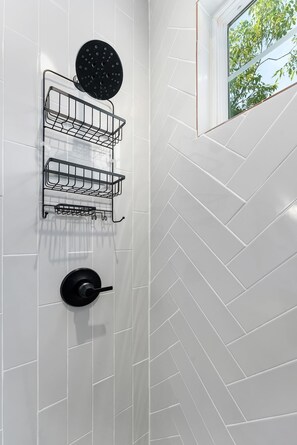 A bathroom with white herringbone-patterned tiles, a black showerhead, and a black circular object on the wall.