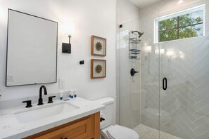 Un baño moderno con un espejo grande, un lavamanos con grifos negros, un inodoro, una ducha con puerta de vidrio y dos adornos enmarcados en la pared.