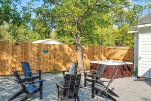 Un patio trasero con cerca de madera, un árbol y dos sillas Adirondack.