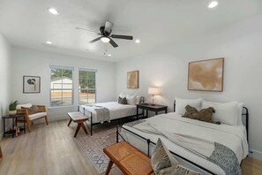 Un dormitorio moderno con dos camas, un ventilador de techo y un ventanal grande.