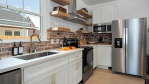 A modern kitchen with white cabinets, a stainless steel refrigerator, a microwave, and a brick backsplash.