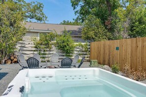 A hot tub with a wooden deck, surrounded by Adirondack chairs and a stone wall.