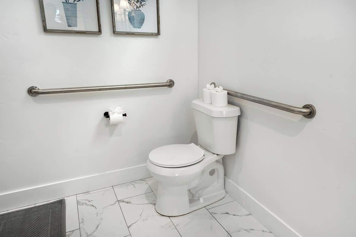 A white bathroom with a toilet, marble floor, and two framed pictures on the wall.