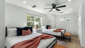 A bedroom with two beds, a ceiling fan, and a large window.