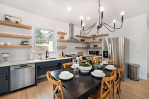 A modern kitchen with a dining area, stainless steel appliances, wooden shelves, and a chandelier. - Southern Vine Sip + Stay Combo (Fredericksburg)